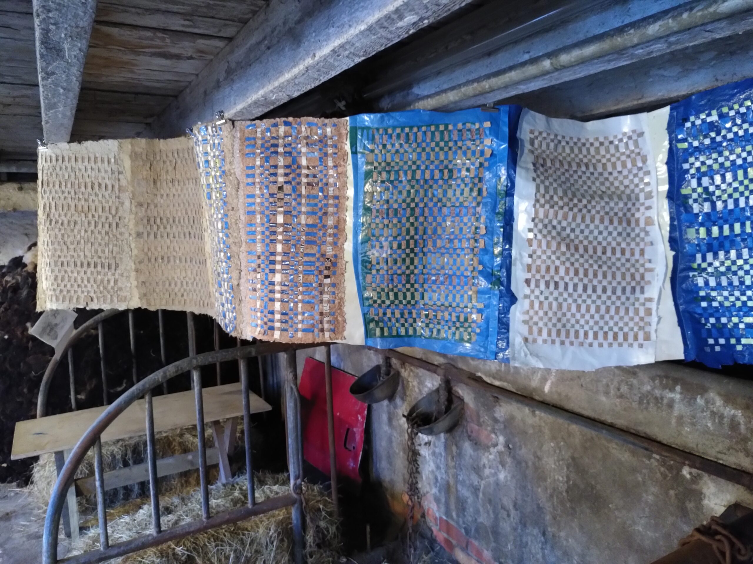 a landscape of woven plastic and paper artworks, stitched together and hung over a feeding area in an old cow barn.