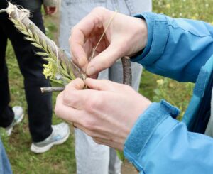 White woman's hands attach grasses to a stick