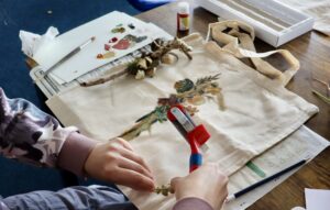 Hands holding a print roller, making a print of a stick with dried flowers